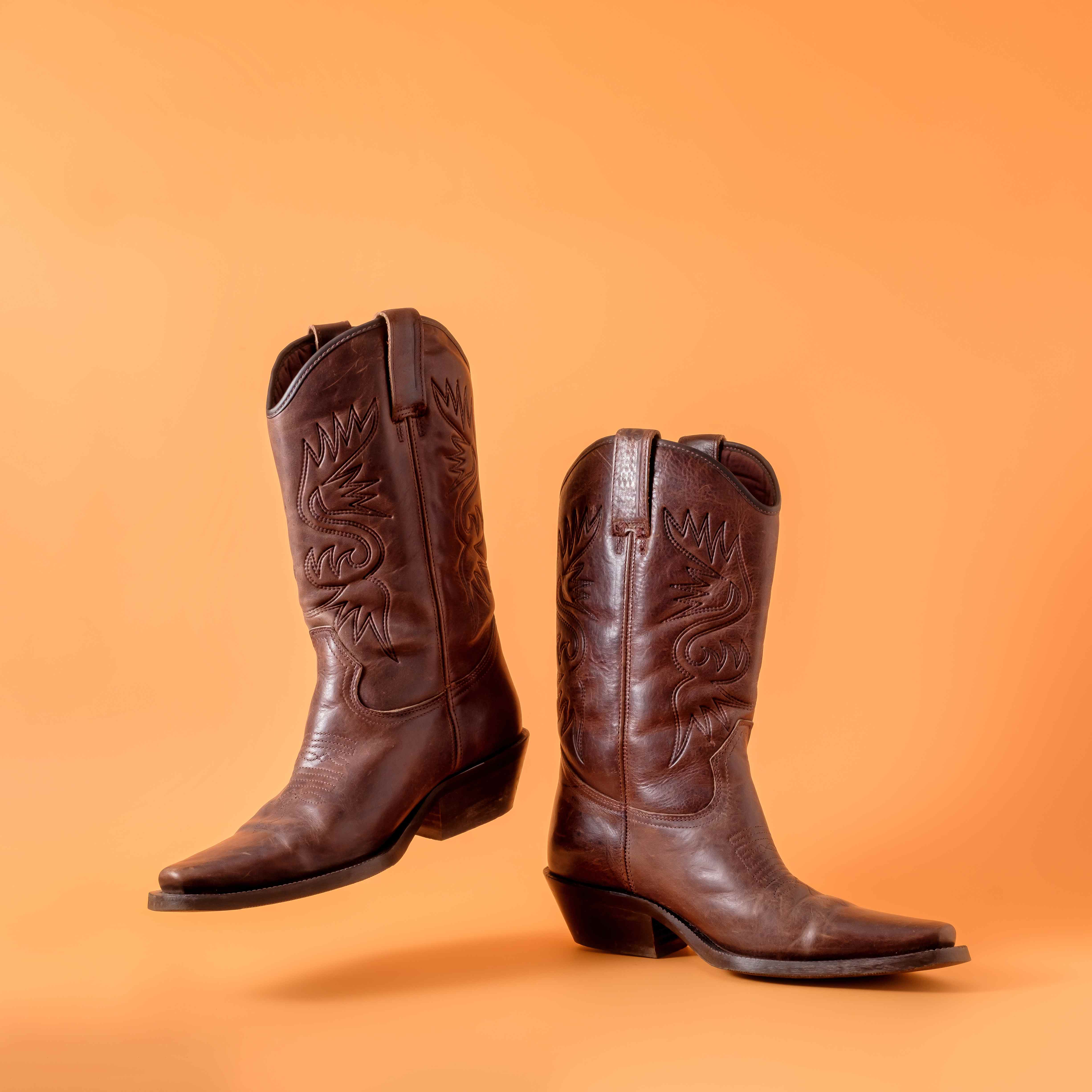 Pair of brown leather cowboy boots on an orange background